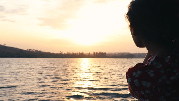 Silhouette féminine accoudée au-dessus de l'eau face au soleil couchant