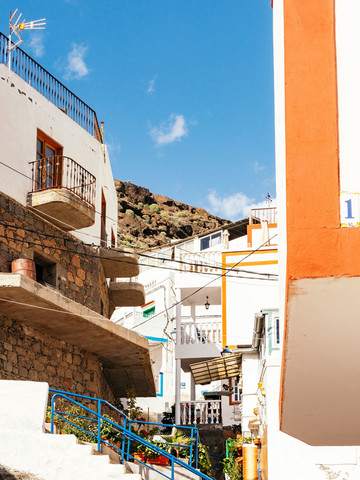 Une ruelle colorée d'une ville canarienne surplombée par la roche volcanique d'une falaise