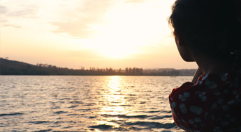 Silhouette féminine accoudée au-dessus de l'eau face au soleil couchant